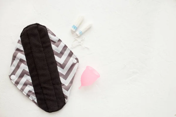 Serbet sanitasi yang dapat dipakai, cangkir menstruasi dan tampon pada latar belakang putih. Konsep periode wanita. Eco ramah dan produk alternatif untuk periode. Letak datar, tilikan atas . — Stok Foto