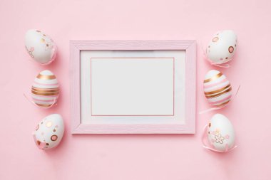 Paskalya pembe yumurtaları ve pembe renkli arka planda beyaz fotoğraf çerçevesi. Mutlu Paskalyalar ve bahar tatilleri kavramı. Üst görünüm, düz görünüm, kopyalama alanı