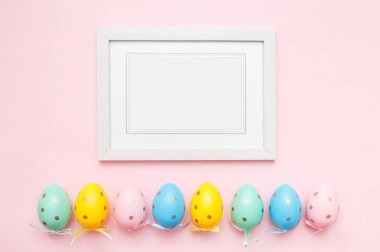 Paskalya yumurtası ve pembe pastel arka planda beyaz fotoğraf çerçevesi. Mutlu Paskalyalar ve bahar tatilleri kavramı. Üst görünüm, düz görünüm, kopyalama alanı