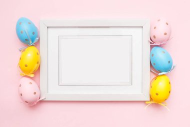 Paskalya yumurtası ve pembe pastel arka planda beyaz fotoğraf çerçevesi. Mutlu Paskalyalar ve bahar tatilleri kavramı. Üst görünüm, düz görünüm, kopyalama alanı