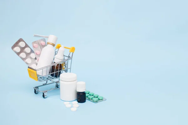 Medicines and pills in a shopping cart on blue background. Drug delivery. Copy space.