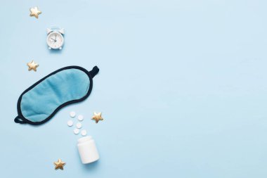 Haplar, şişe, uyku maskesi ve mavi pastel arka planda yıldızlı beyaz alarm saati. Insomnia kavramı, uyku sorunları, ilaç alıp tedavi olma zamanı. Üst görünüm, düz görünüm, kopyalama alanı.