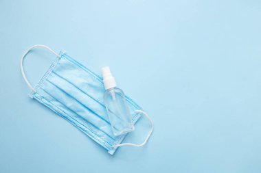 Doktor için maske ve sprey alkol. Mavi pastel arka plan üzerinde Covid-19 virüs konsepti. Düz konum, üst görünüm, kopyalama alanı.