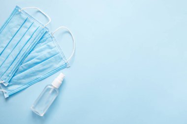 Doktor için maske ve sprey alkol. Mavi pastel arka plan üzerinde Covid-19 virüs konsepti. Düz konum, üst görünüm, kopyalama alanı.