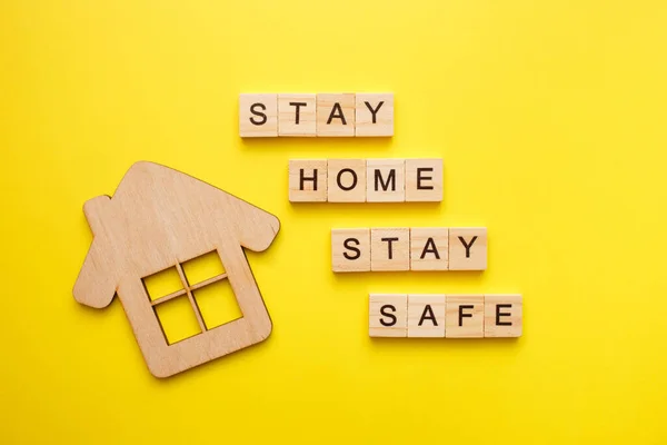 Stay Home tekst z drewnianym domu na żółtym tle. Koncepcja kwarantanny, ochrona przed wirusami. Widok z góry, płaski. — Zdjęcie stockowe