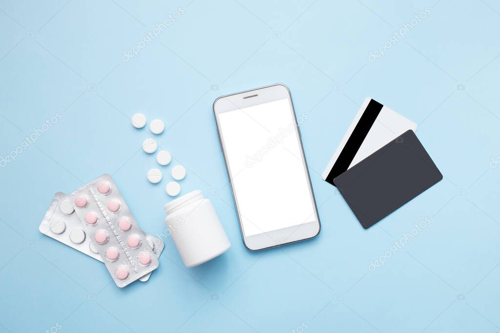 Smartphone with pills and credit card on a blue background. Stay home concept. Pharmacy online shopping. Flat lay, top view
