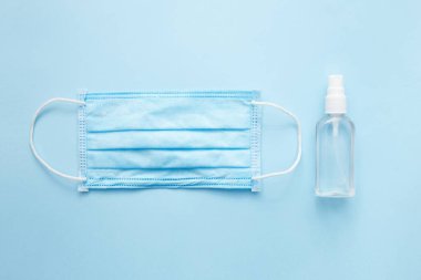 Doktor için maske ve sprey alkol. Mavi pastel arka plan üzerinde Covid-19 virüs konsepti. Düz yatış, üst görünüm.