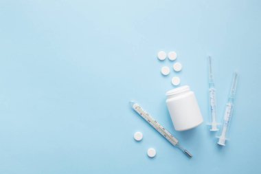 Haplar mavi arka planda şırınga termometresinden dökülüyor. Virüs koruma konsepti. Düz konum, üst görünüm, kopyalama alanı.
