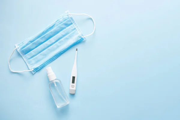 Maske, dijital termometre ve doktor için sprey alkol. Mavi pastel arka plan üzerinde Covid-19 virüs konsepti. Düz konum, üst görünüm, kopyalama alanı