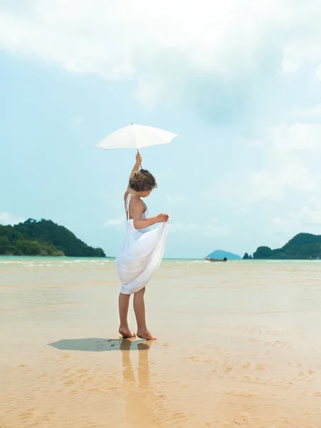 Menina em vestido branco com guarda-chuva renunciando na praia — Fotografia de Stock