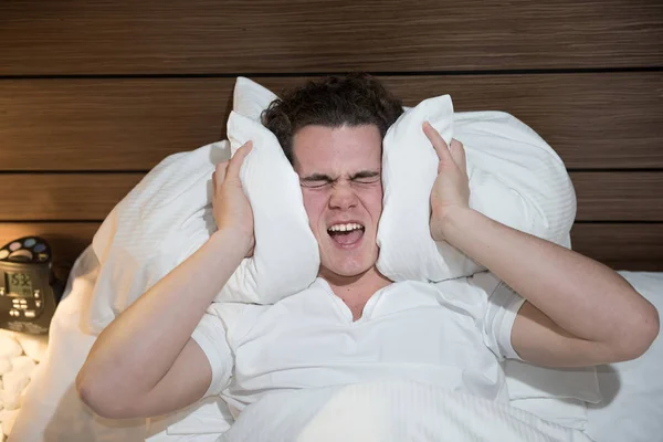 Jeune homme caucasien dans le mauvais sommeil tenant oreiller silence bruit — Photo
