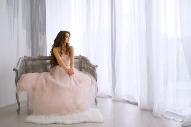 Güzel kız pembe elbiseli pencerenin yanında oturuyor.