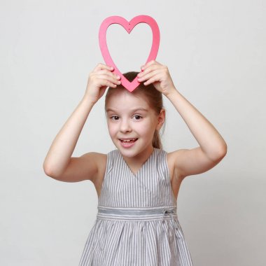 Ahşap kalp sembol tatil tema üzerinde tutan çekici ve neşeli küçük kız