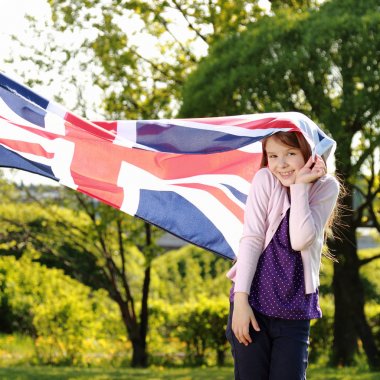 Açık havada büyük bir Britanya bayrağı tutan bir parkta Kafkas neşeli sevimli kız ayakta