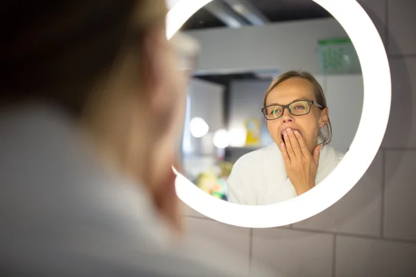 Groggy, ung kvinna gäspningar framför hennes badrumsspegel — Stockfoto