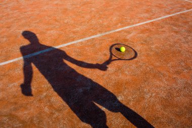 Tenis kortunda oynayan bir tenisçinin gölgesi