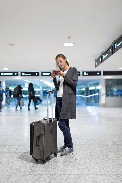 Genç bir kadın yolcu havaalanında, tablet bilgisayarını kullanarak — Stok fotoğraf