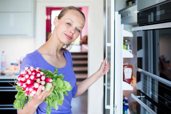 Mulher bonita e jovem tirando vegetais frescos de seu frigorífico — Fotografia de Stock