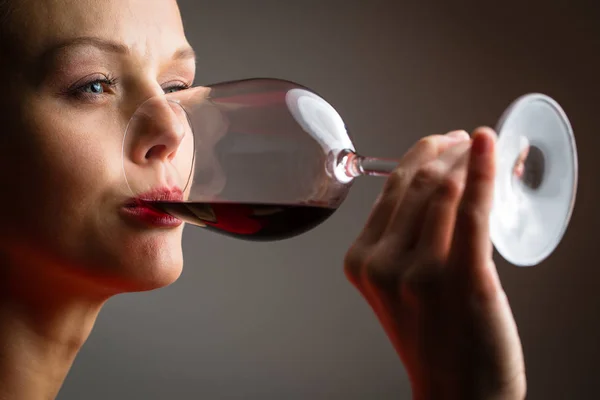 Elegante joven con un vestido rojo, tomando una copa de vino tinto — Foto de Stock