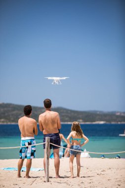 Gençler bir dron uzaktan kumanda ile bir plajda uçan.