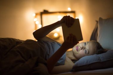 Gece geç saatlerde onun yatağında tablet bilgisayarını kullanan genç kadın 