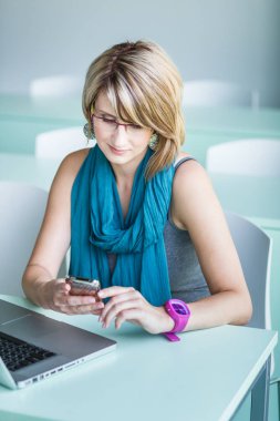 Güzel genç bayan bir dizüstü bilgisayar ve onun smartph kullanarak bir ofis,