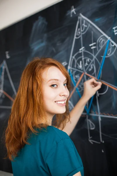 Porträt einer hübschen jungen Studentin, die an die Tafel schreibt — Stockfoto