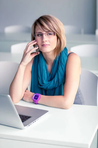 Bonita, joven mujer en una oficina, usando un portátil y su smartph —  Fotos de Stock