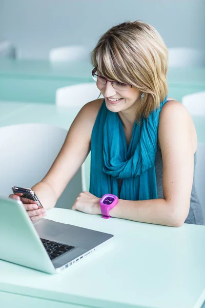 Bonita, joven mujer en una oficina, usando un portátil y su smartph —  Fotos de Stock