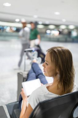 genç bir kadın yolcu havaalanında, tablet bilgisayarını kullanarak