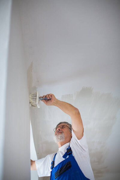 Senior painter man at work with a paint bucket, wall painting co