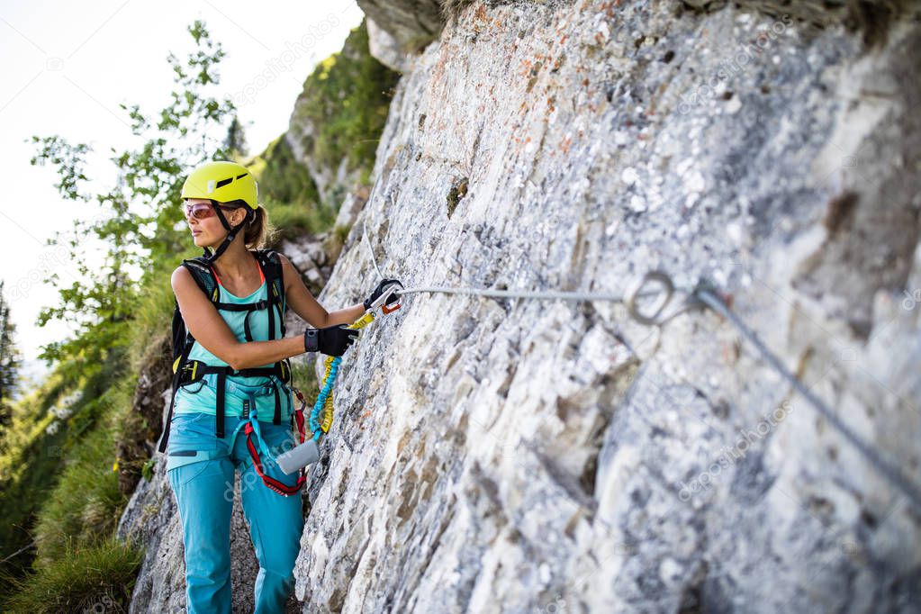 Pretty, female climber on a via ferrata -  climbing on a rock in