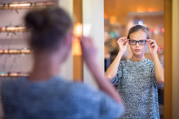 Vacker, ung kvinna att välja nya glasögon ramar i en optiker butik — Stockfoto