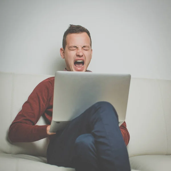 Schläfriger junger Mann sitzt auf einem Sofa und versucht es — Stockfoto