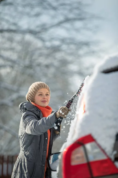 Mujer bonita y joven limpiando su coche de la nieve después de una fuerte tormenta de nieve — Foto de Stock