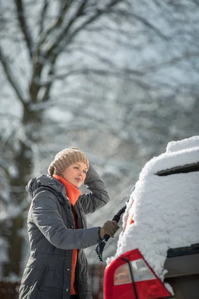 Güzel, genç bir kadın yoğun kar fırtınasından sonra arabasını kardan temizliyor. — Stok fotoğraf