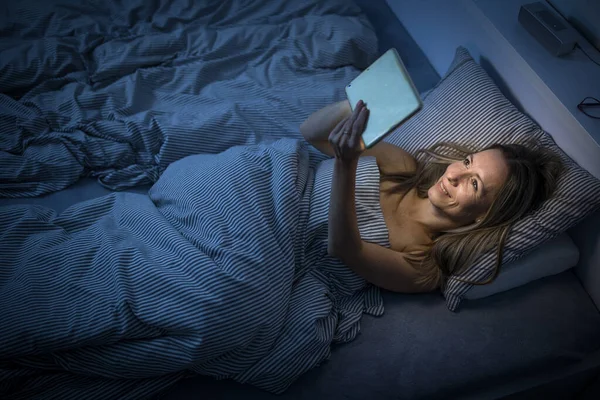 Wanita cantik setengah baya menggunakan komputer tabletnya sebelum tidur — Stok Foto