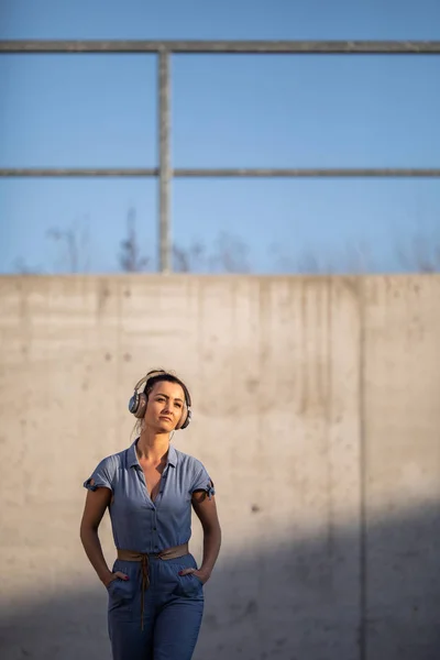 Jolie, jeune femme avec écouteurs debout contre le mur de béton — Photo