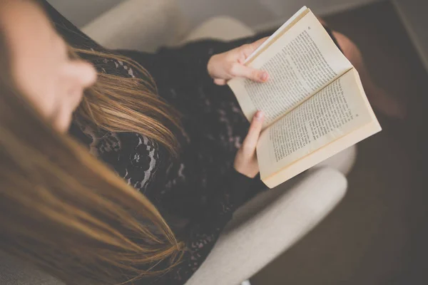 Nette junge Frau liest ein Buch im Designerstuhl — Stockfoto