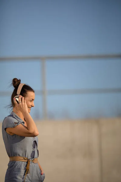 Mooie, jonge vrouw met hoofdtelefoon staande tegen betonnen muur — Stockfoto