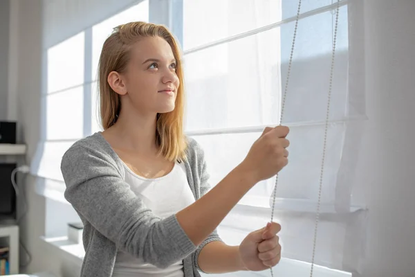 Pretty, young woman lowering the interior shades/blinds — Stockfoto