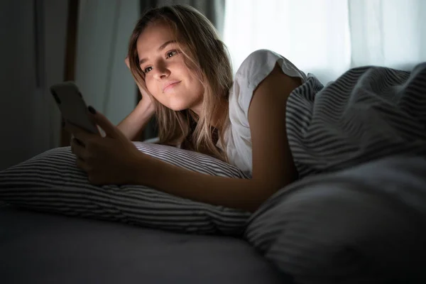 Hezká mladá žena v posteli s mobilním telefonem — Stock fotografie