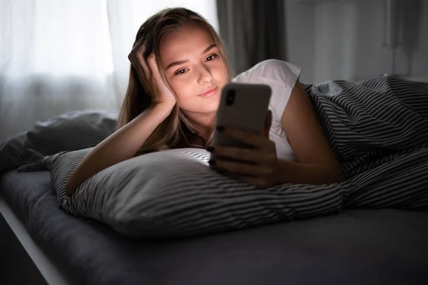 Pretty, young woman in her bed with her cell phone — Stockfoto