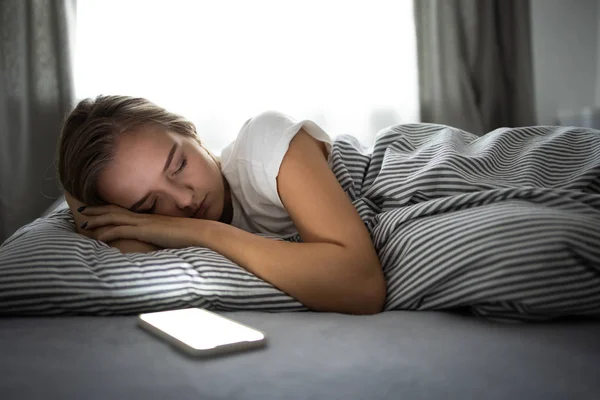 Hübsche, junge Frau schläft mit ihrem Handy im Bett — Stockfoto