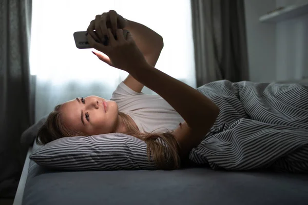 Mujer bonita y joven durmiendo en su cama con su teléfono celular —  Fotos de Stock