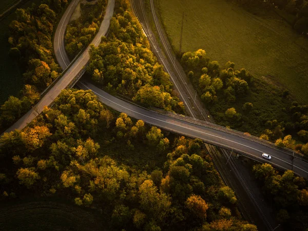 Větrná cesta v podzimním lese při západu slunce v horách — Stock fotografie