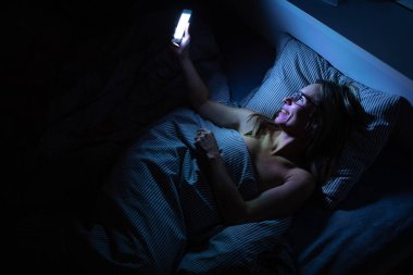 Yatakta cep telefonunu kullanan orta yaşlı güzel bir kadın. 