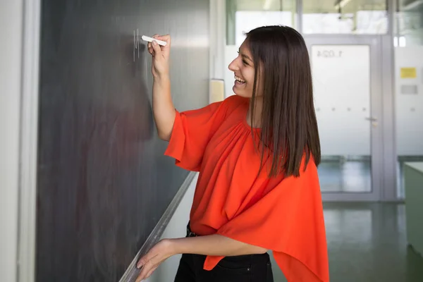 Mooie, jonge student / jonge leraar die op het schoolbord schrijft — Stockfoto