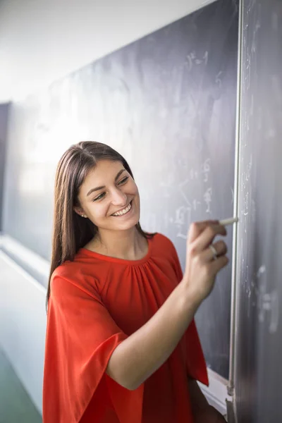 Ładna, młoda studentka / młoda nauczycielka pisząca na tablicy — Zdjęcie stockowe