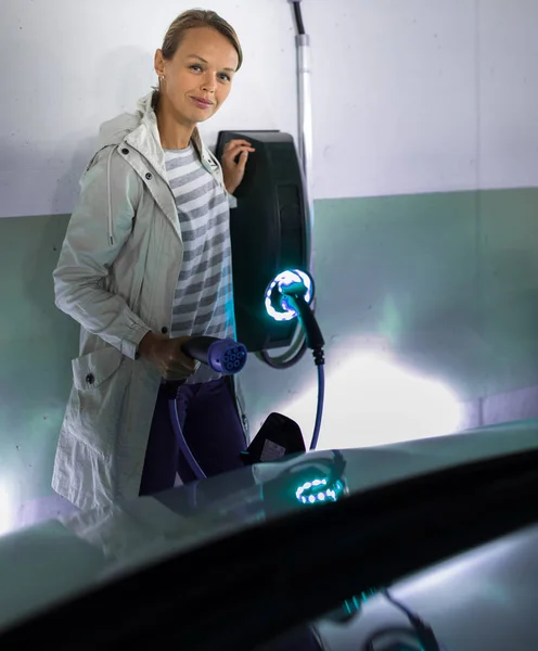 Mujer joven cargando un vehículo eléctrico en un garaje subterráneo — Foto de Stock